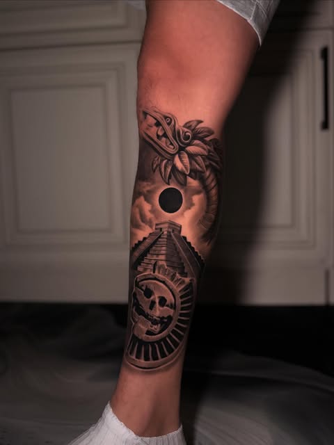 Black-and-grey Mayan-inspired leg tattoo with pyramid, eclipse and sculpted face