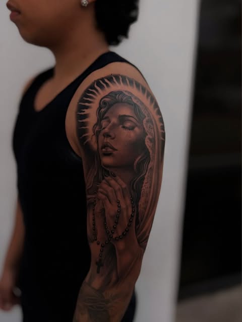 Detailed black-and-grey praying woman tattoo on an upper arm