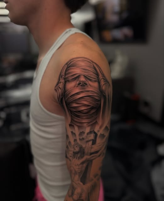 Black-and-grey wrapped face tattoo extending across an upper arm