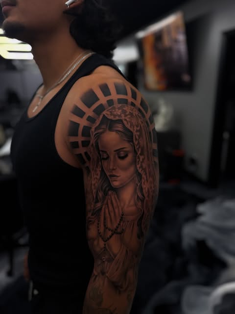Black-and-grey praying woman tattoo with geometric halo on an upper arm